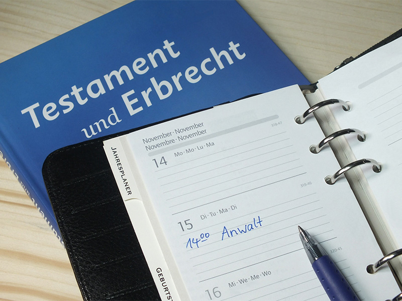 Kalender mit Termineintrag Anwalt, Kugelschreiber und Fachbuch zu Testament und Erbrecht für Informationen zum Testament in Lörrach.
