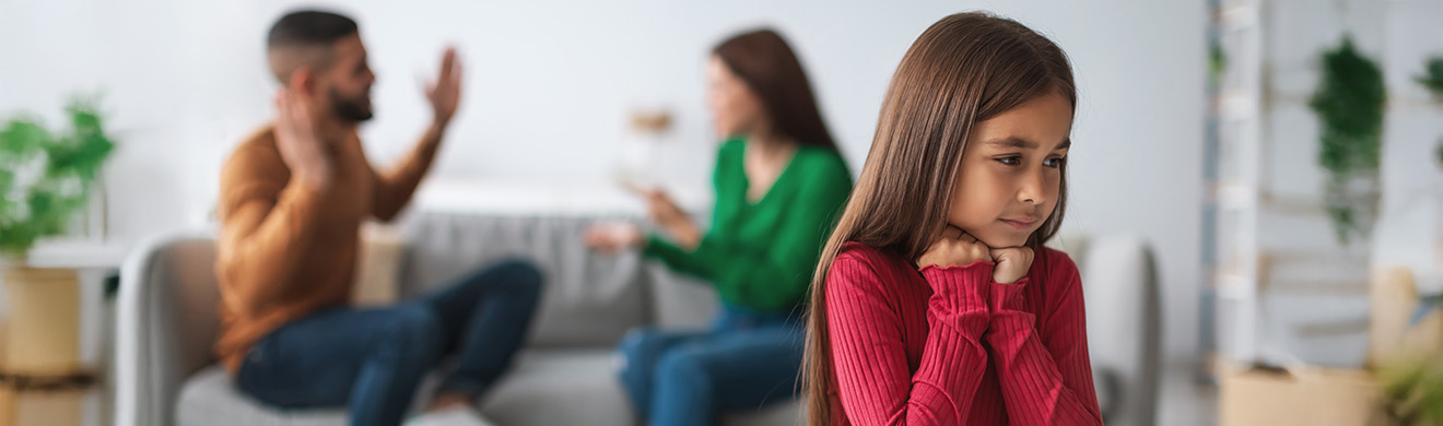 Trauriges Kind sitzt im Vordergrund, während die Eltern im Hintergrund über ihre Trennung streiten und familiäre Spannungen sichtbar werden.