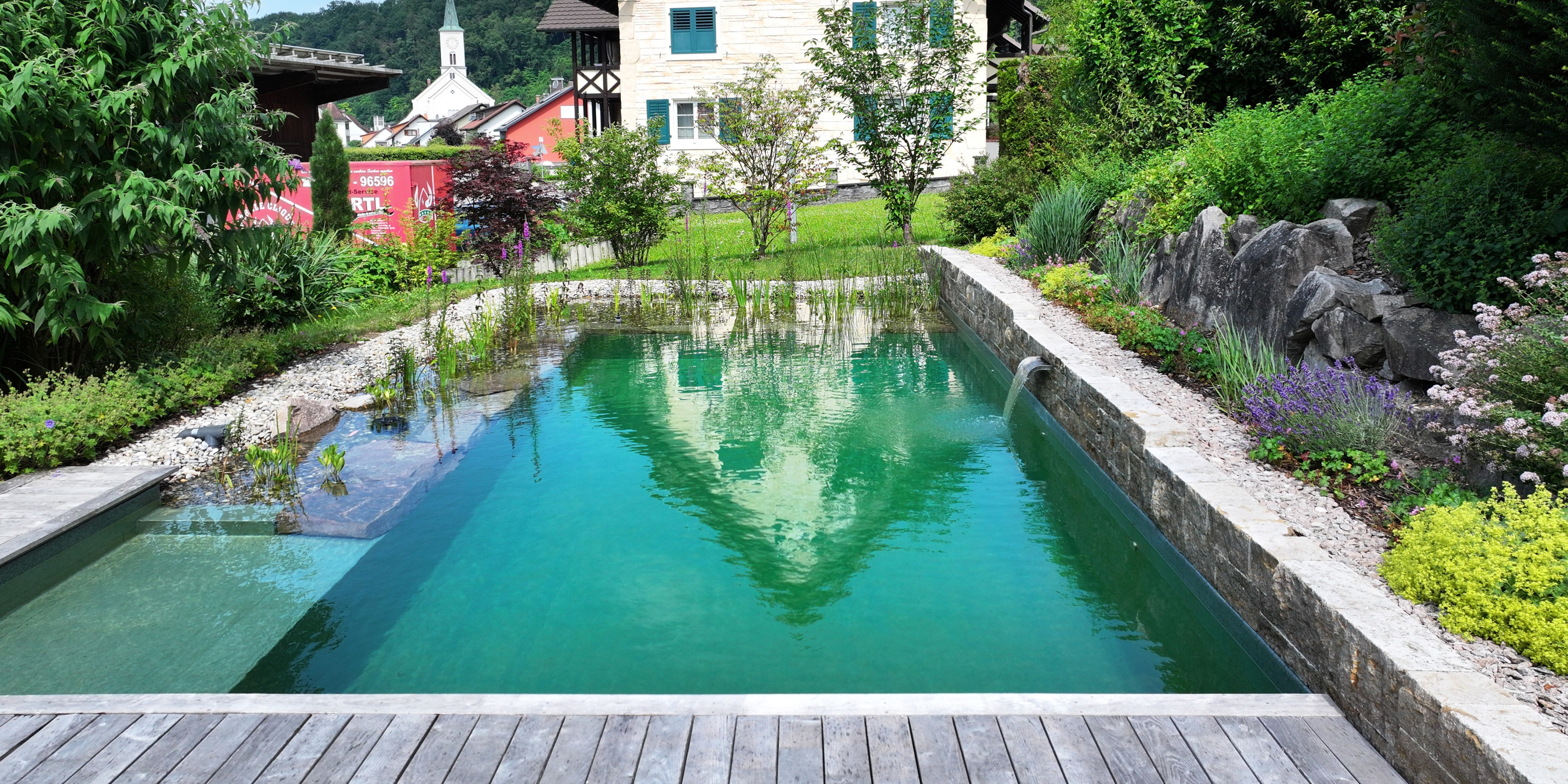 Naturnaher Schwimmteich mit integriertem Wasserspiel, üppiger Bepflanzung und harmonisch gestalteter Gartenanlage in Weil am Rhein.