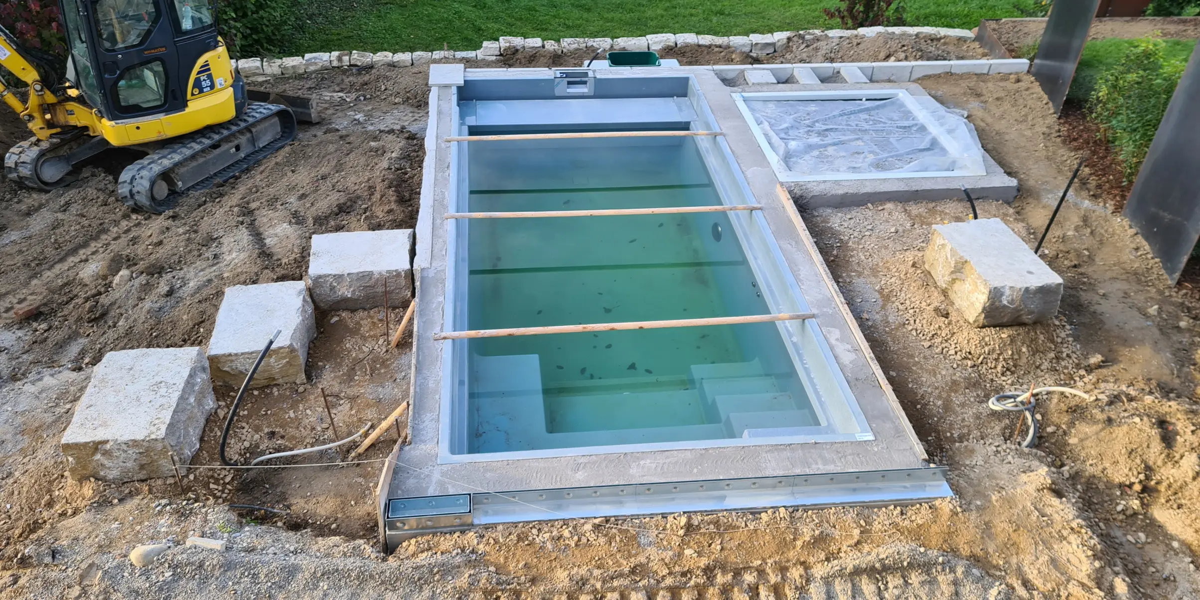 Bereits eingebauter Pool im Rohbau mit noch nicht fertiggestelltem Gartenbereich bei einem Poolbauprojekt in Weil am Rhein.